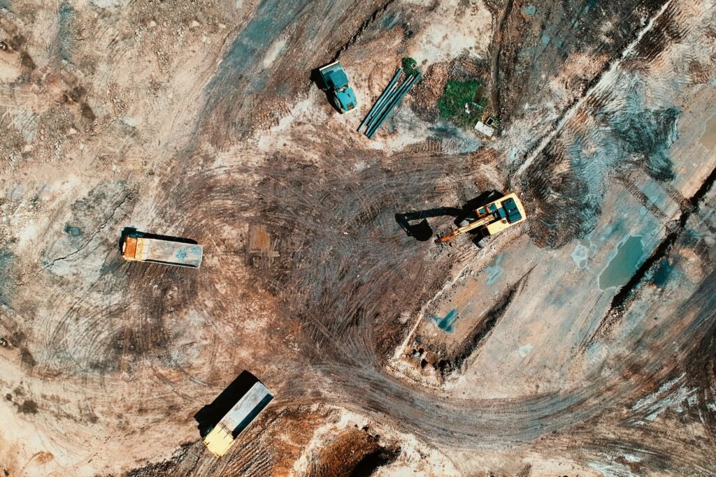 High-angle aerial view of construction site with earthmoving equipment and trucks.